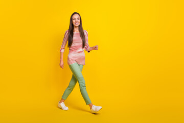 Fototapeta na wymiar Photo of shiny charming young woman wear striped shirt smiling walking empty space isolated yellow color background