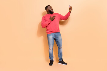 Full size photo of cool young brunette guy video call wear pink pullover jeans shoes isolated on beige background