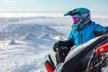a snowmobiler is resting on top of a mountain, tipping the snowmobile on its side. snowmobile...