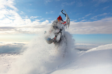 elite sports snowmobiler rides and jumps on steep mountain slope with swirls of snow storm. a trail of splashes of white snow. bright snowmobile and suit without brands