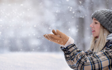 Young woman catches snowflakes buzzing in a winter forest. She rejoices in the snow and catches...