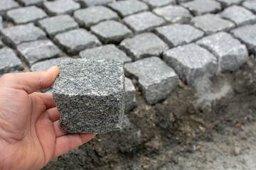 worker holds rectangular quarried stone used in paving streets, a sett