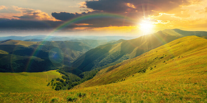 mountain landscape in summer at sunset. grassy meadows on the hills rolling in to the distant peak beneath a rainbow in evening light