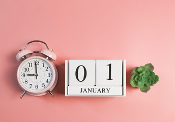 wooden calendar 01 January, pink vintage alarm clock 9 o'clock and succulent plant pot on pink background. First morning of new year.