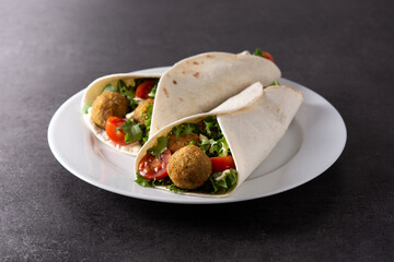 Tortilla wrap with falafel and vegetables on black stone background