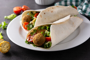 Tortilla wrap with falafel and vegetables on black stone background
