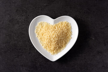 Raw rice on heart shaped plate on black background. Top view.