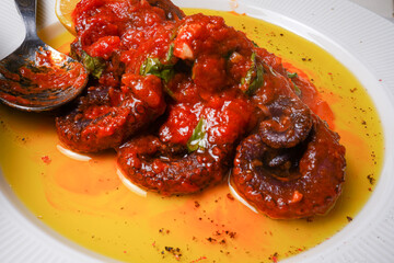 Octopus in tomato sauce with basil, oil and lemon serving in white plate. Top view