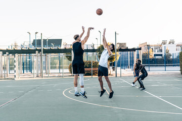 Friends jumping while playing basketball between friends in an urban outdoor court
