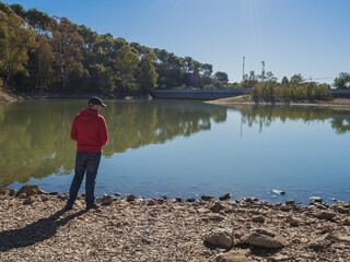 Fototapeta na wymiar A young man in a red sweatshirt walks alone looking at the landscape with a lake