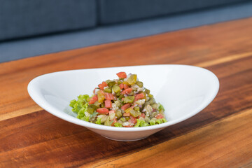 Traditional Russian Christmas and New year salad Olivier on white plate on wooden background. Top view, close up with copy space. High quality photo