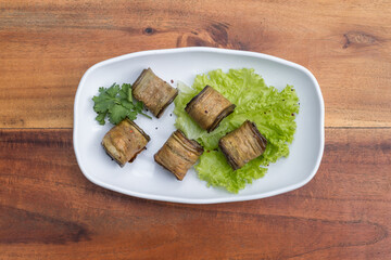 Eggplant rolls decorated with fresh lettuce and parsley on white plate, wooden background. Top view, close up with copy space, Georgian cuisine. 