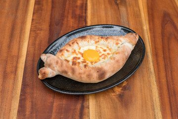 Traditional Georgian cuisine. Ajara khachapuri with egg on black plate on wooden background Top view, close up with copy space. High quality photo