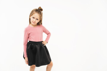 A girl in a pink blouse and a black skirt. Cute girl with blonde hair. Fashionable child on a light background. The child has hands on his belt