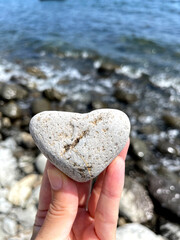 Heart shape stone in girls hand against background of beach. Summer sunny day. Love, wedding and Valentine day concept. Finding beautiful and interesting stones. Beach vacation