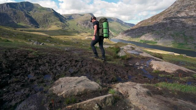 A backpacker hiking through thick mud in the mountains with large pack