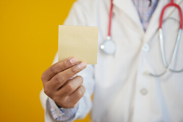  doctor hand hold a sticky note against yellow background 