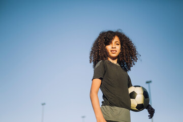 Ambitious girl standing with soccer ball against clear sky