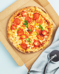 Tasty Italian big pepperoni pizza with thin dough, salami, mozzarella, cherry tomatoes and basil in a craft box on a blue background with copy space. Mediterranean cuisine. Pizza delivery. Flat lay