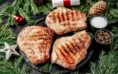 Grilled Christmas Pork Steaks
 with spruce and Christmas decorations on a stone background 