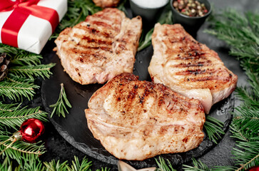 Grilled Christmas Pork Steaks
 with spruce and Christmas decorations on a stone background