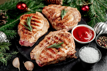 Grilled Christmas Pork Steaks
 with spruce and Christmas decorations on a stone background 