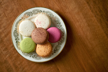 Variety of flavors of macaroon pastries in a white plate on a wooden background. Close up,...