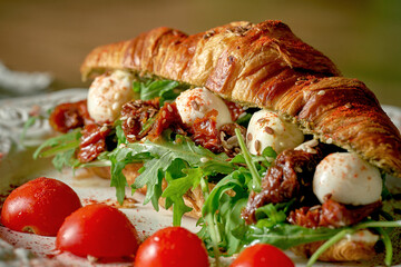 Croissant sandwich with sun-dried tomatoes, arugula, mozzarella in a white plate on a wooden background
