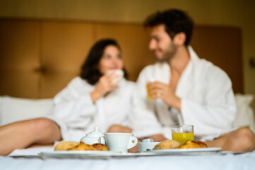 Obraz na płótnie Canvas Beautiful couple have breakfast on bed in hotel, young man and woman in bathrobes happy together in the morning