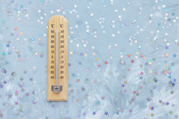 Thermometer shows low plus temperature and confetti decoration on white and blue with stars festive background. Christmas weather concept, copy space