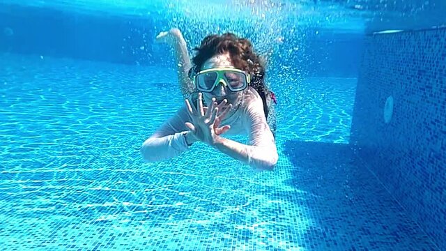 The girl swims underwater in the pool wearing a mask.