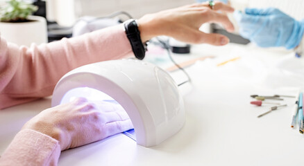Woman in manicure salon drying her nails in a UV lamp