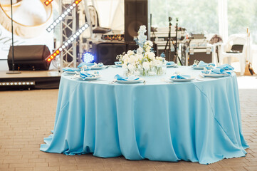 Wedding tables for guests. Round tables with a blue tablecloth. Decorated with flowers, plates, glasses and more