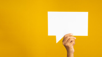 Hand holding of an empty white speech bubble against a yellow background