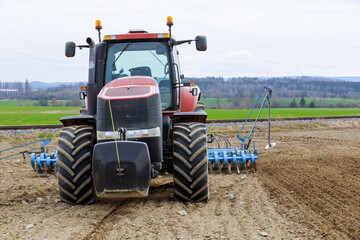 Obraz premium Complex of spring field works. A tractor with a seed drill in a field near the railway. Agro-industrial business.