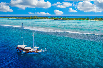 Small yacht sailing in tropical sea over coral reef in Indian ocean lagoon. Exotic island...