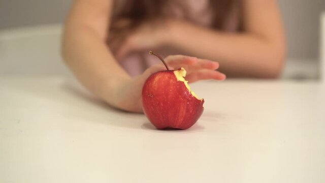 The child refuses to eat healthy food. A little girl pushes an apple away. Close-up of a bitten apple.
