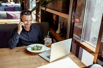 businessman is talking on phone, while having lunch and working on laptop in restaurant. remote work.