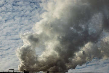 White and gray smoke and steam from a high concrete chimney against the bright blue sky