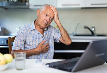 A modern elderly man is sitting at home, conducting an online consultation with a doctor on a...
