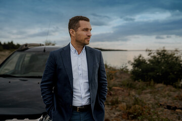 Young handsome man with black classic car wearing black suit. Man is standing near his car outdoors.