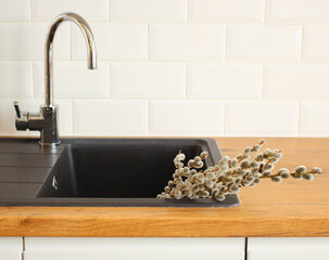 Closeup of kitchen interior. White brick wall, metro tiles. Goat willow in the black sink. Modern...