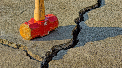 Old wooden sledgehammer on a broken cracked concrete slab under the sunlight