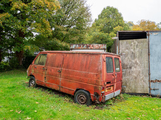 Old red weathered damaged dirty van parked on a grassy ground in nature