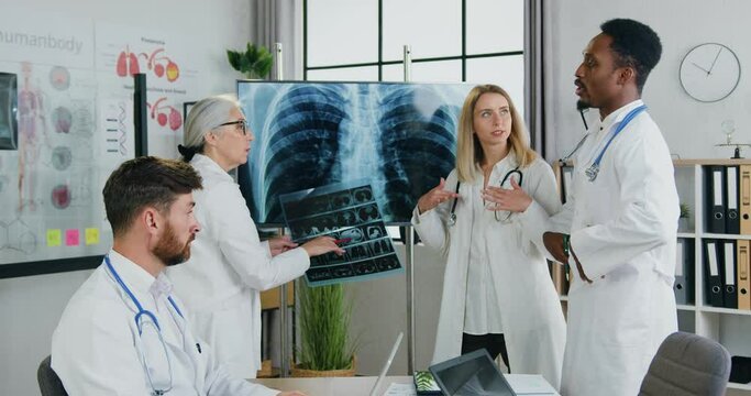 Workflow in clinic where pleasant successful high-skilled multicultural male and female doctors holding meeting and discussing results of chest and lungs x-ray,front view