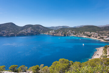 Fototapeta premium Panoramic of the bay of Camp de Mar, Mallorca. Blue Mediterranean sea and sky. Pine trees around and boats in the sea.