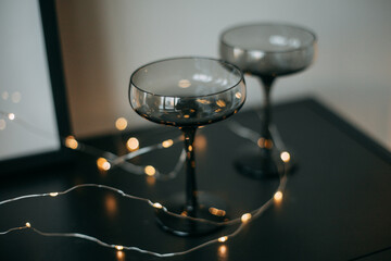 At home, on the table are glasses made of dark glass with lighting from a garland. Interior details