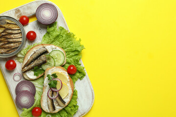 Board with sandwiches with sprats on yellow background