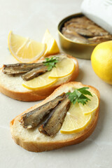 Sandwiches with sprats and ingredients on light background