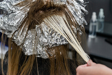 Hair stylist checking models hair during bleaching process. Trendy hair lightening using shatush...